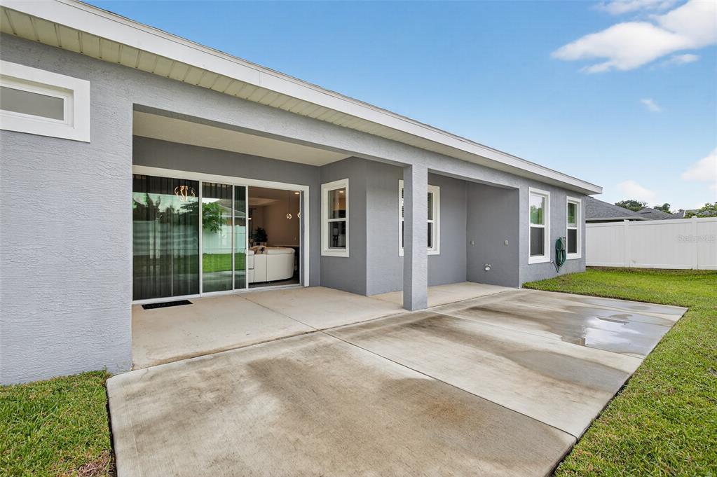 A gray house exterior features a concrete patio, sliding glass doors, and a white fence — 46 FURNESS PLACE, PALM COAST, FL