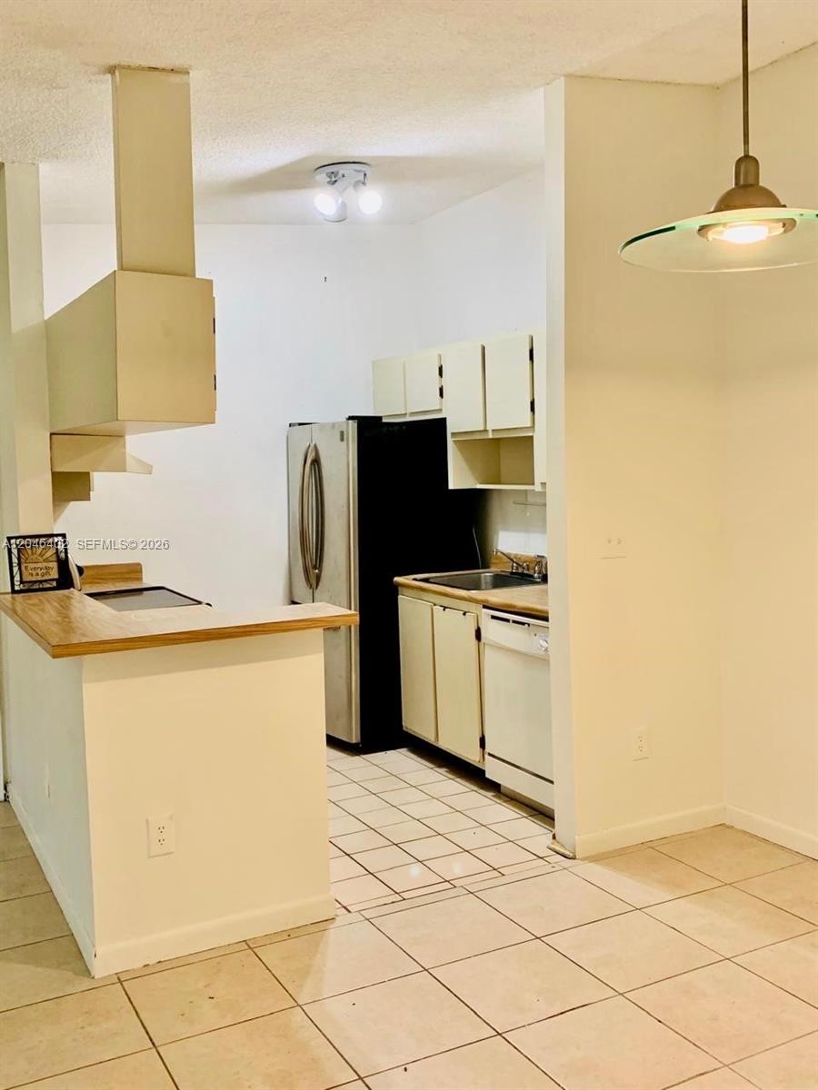 A kitchen features white cabinets, a black refrigerator, a dishwasher, and a tiled floor — 809 NE 199th St # 7, Miami FL 33179, MIAMI, FL