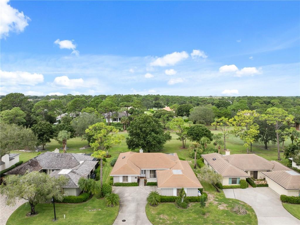 An aerial view shows three suburban houses with tiled roofs surrounded by trees and grass — 110 Prestwick Circle, Vero Beach FL 32967, VERO BEACH, FL