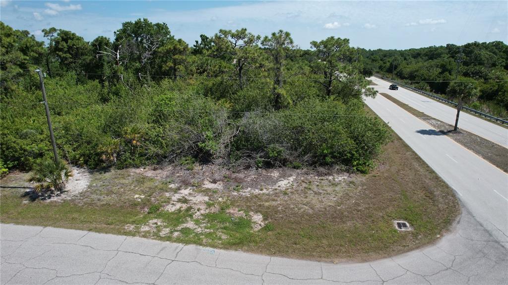 An aerial view shows a vacant, wooded corner lot adjacent to a paved road — 142 LOMAS ROAD, ROTONDA WEST, FL