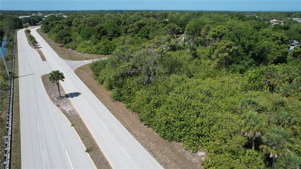 An aerial view shows a paved road running alongside a dense, wooded vacant lot — 142 LOMAS ROAD, ROTONDA WEST, FL