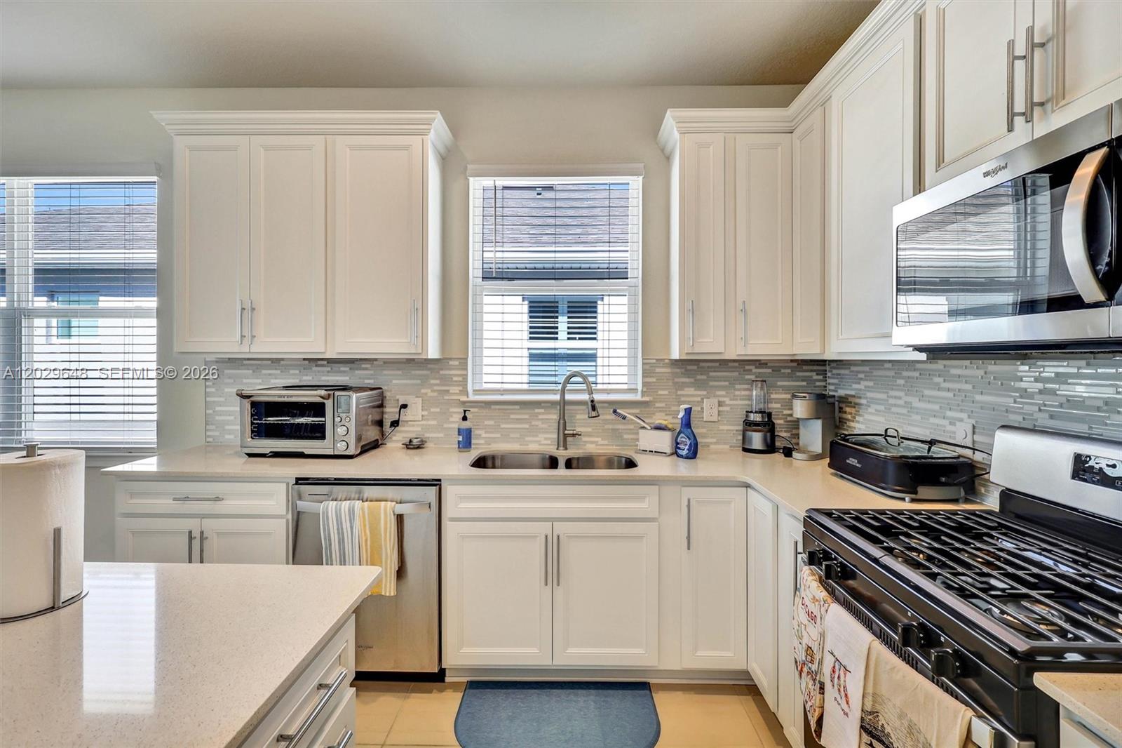 A kitchen features white cabinets, stainless steel appliances, a double sink, and a tiled backsplash — 15806 GEM VIEW ST, Winter Garden FL 34787, WINTER GARDEN, FL