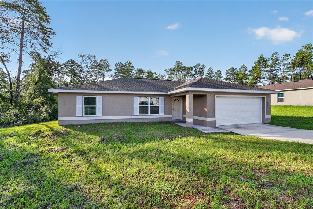 A single-story house with a tan stucco exterior, white shutters, and an attached two-car garage — 16993 SW 20 COURT ROAD, OCALA, FL