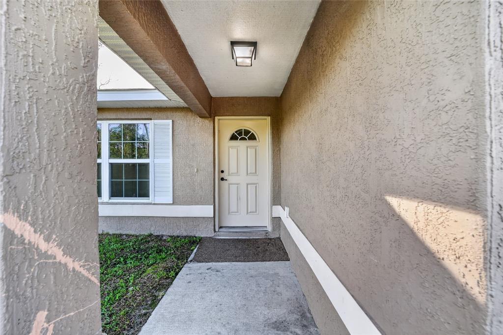 A beige stucco house exterior features a front door, a window, and a concrete walkway — 16993 SW 20 COURT ROAD, OCALA, FL