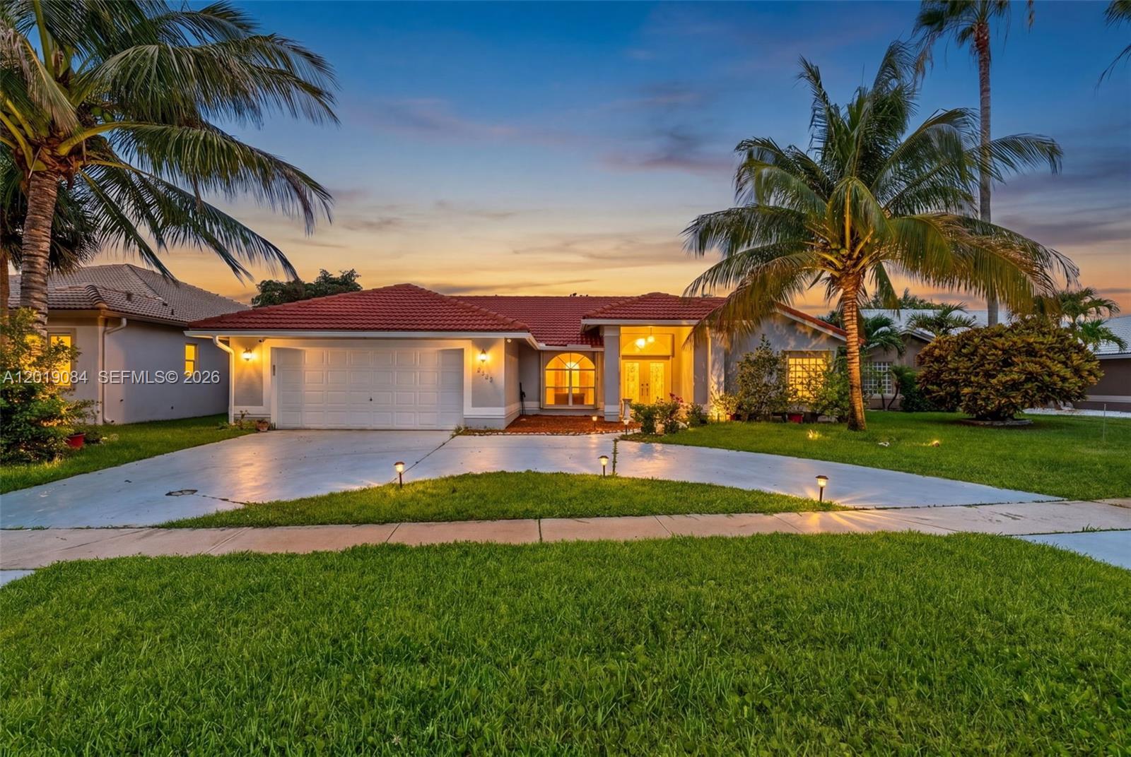 A single-story house with a red tile roof, white garage, and palm trees at dusk — 3462 Harness Cir, Wellington FL 33449, WELLINGTON, FL