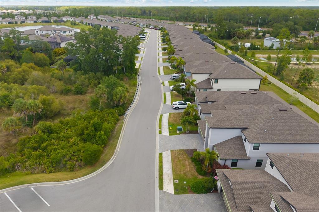 An aerial view shows a suburban street lined with townhomes and adjacent wooded areas — 19524 FISHHAWK TRAIL, VENICE, FL
