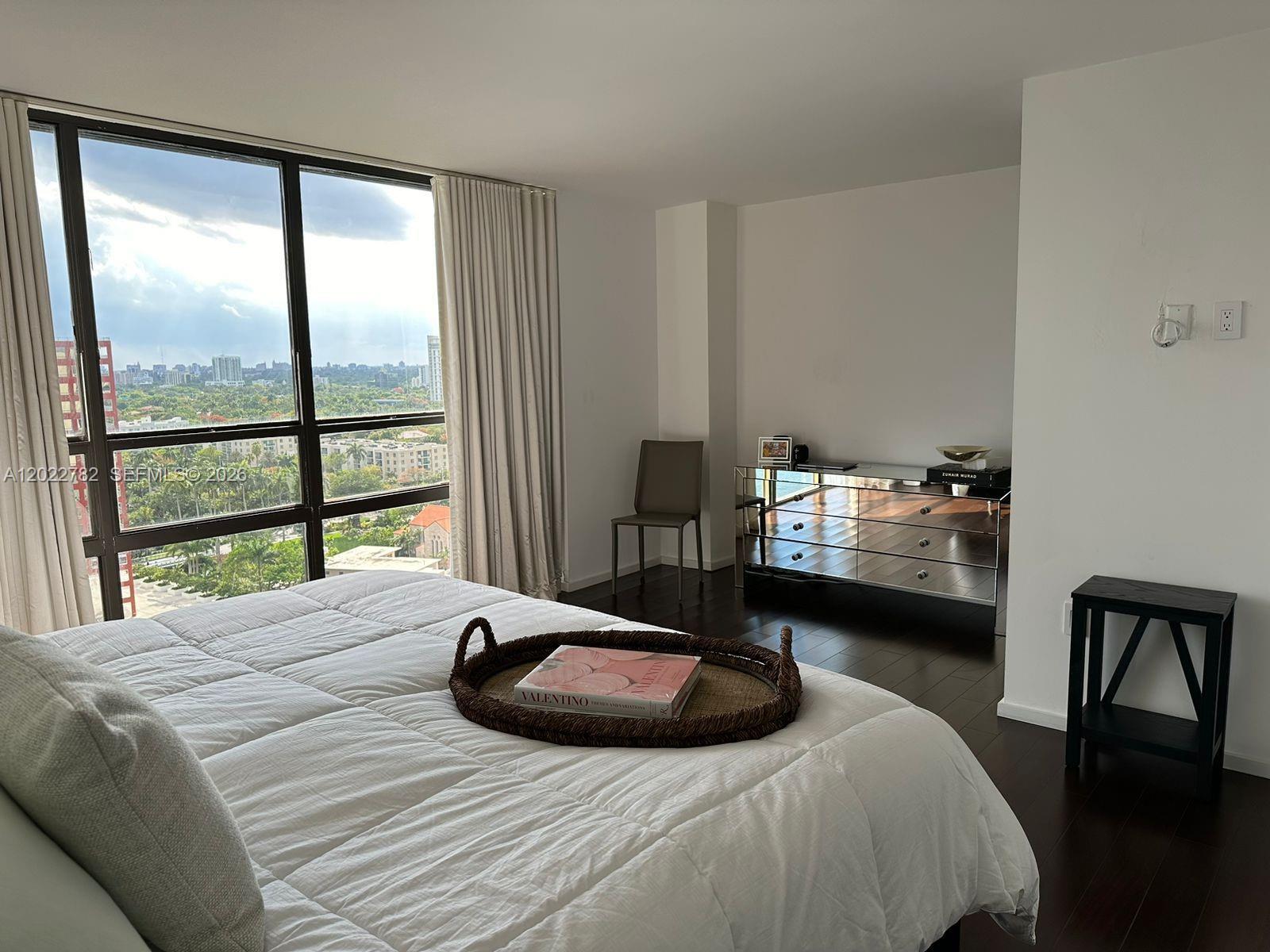 A bedroom with a white bed, mirrored dresser, and floor-to-ceiling windows overlooking a city view — 1450 Brickell Bay Dr # 1907, Miami FL 33131, MIAMI, FL