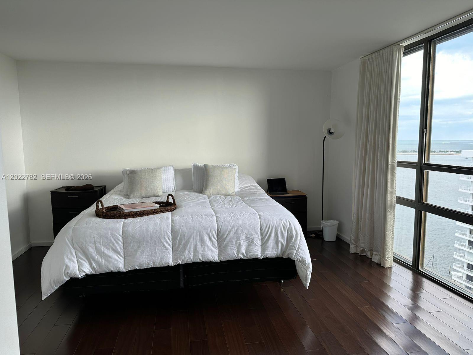 A bedroom features a bed, dark wood floors, and floor-to-ceiling windows overlooking the ocean — 1450 Brickell Bay Dr # 1907, Miami FL 33131, MIAMI, FL