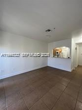 An empty room with tan tile flooring and a pass-through opening to a kitchen — 7995 NW 8th St # 115, Miami FL 33126, MIAMI, FL