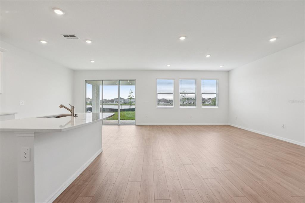 An open-concept living area features light wood-look flooring, recessed lighting, and a kitchen island — 5384 CLOUDBERRY AVENUE, LAKELAND, FL