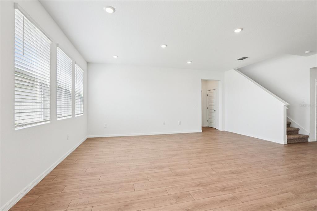 A bright, empty living room features light wood-look flooring, white walls, and a staircase — 5384 CLOUDBERRY AVENUE, LAKELAND, FL