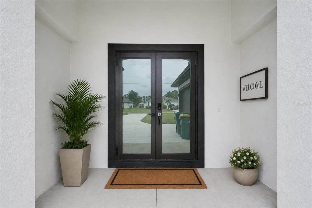 A front entryway features double glass doors, a potted plant, a welcome sign, and mat — 153 AUSTRALIAN DRIVE, ROTONDA WEST, FL