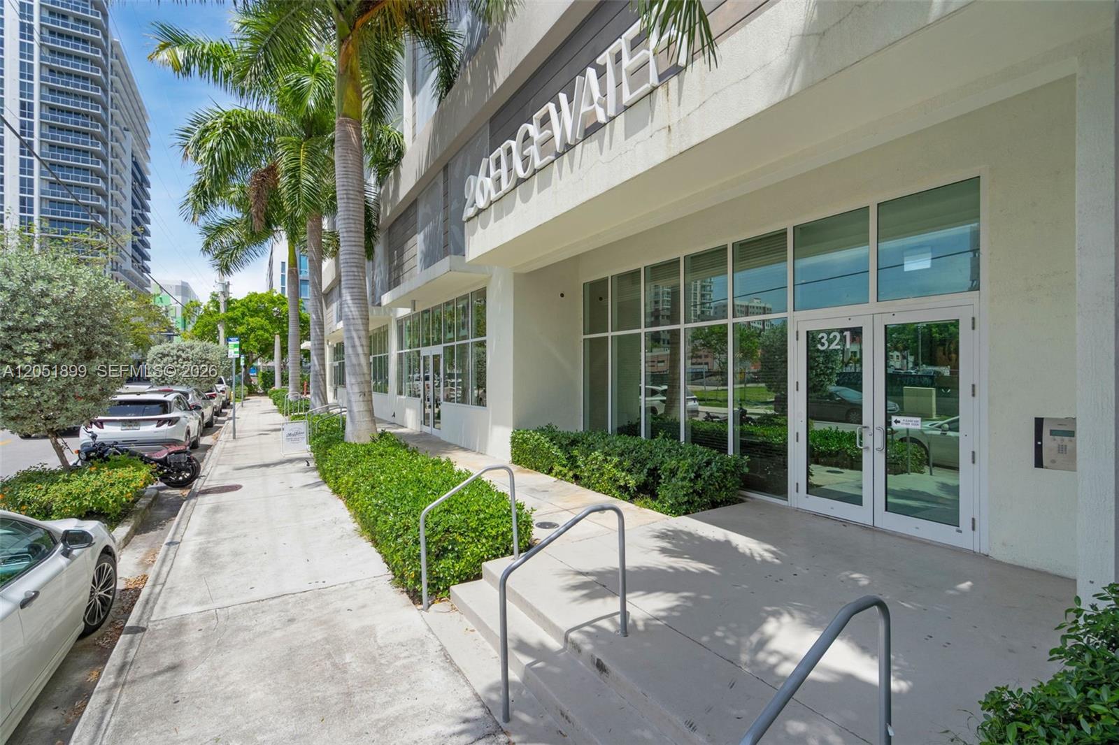 The exterior of a modern building features a glass entrance, palm trees, and a sidewalk — 321 NE 26th St # 709, Miami FL 33137, MIAMI, FL