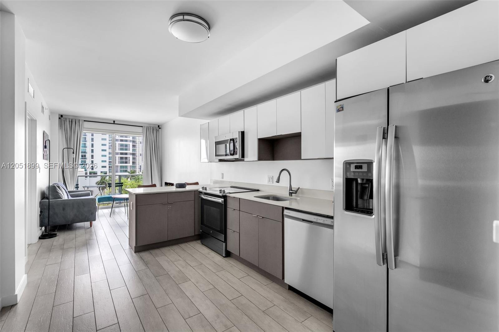A modern kitchen with stainless steel appliances and gray cabinets opens into a living area — 321 NE 26th St # 709, Miami FL 33137, MIAMI, FL