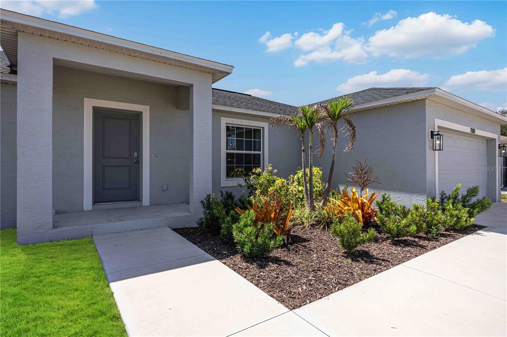 The exterior of a single-story house features a gray facade, a front door, and landscaping — 7089 PLANTATION STREET, ENGLEWOOD, FL
