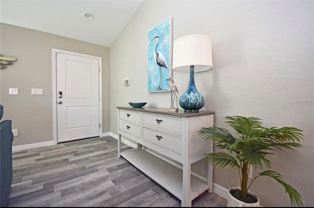 An entryway features a white console table, a blue lamp, a heron painting, and wood-look flooring — 7089 PLANTATION STREET, ENGLEWOOD, FL