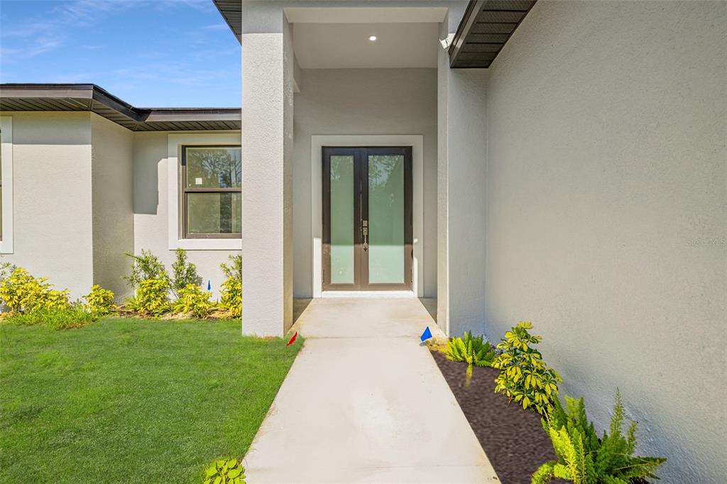 A concrete walkway leads to the double front doors of a modern stucco home — 355 MILTON STREET, PORT CHARLOTTE, FL