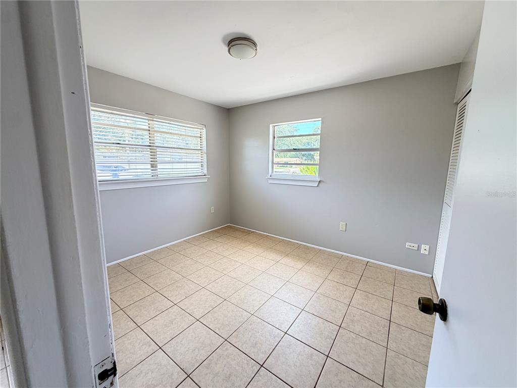 An empty bedroom features light gray walls, beige tile flooring, and two windows with blinds — 3842 HAWKEYE CIRCLE, SARASOTA, FL