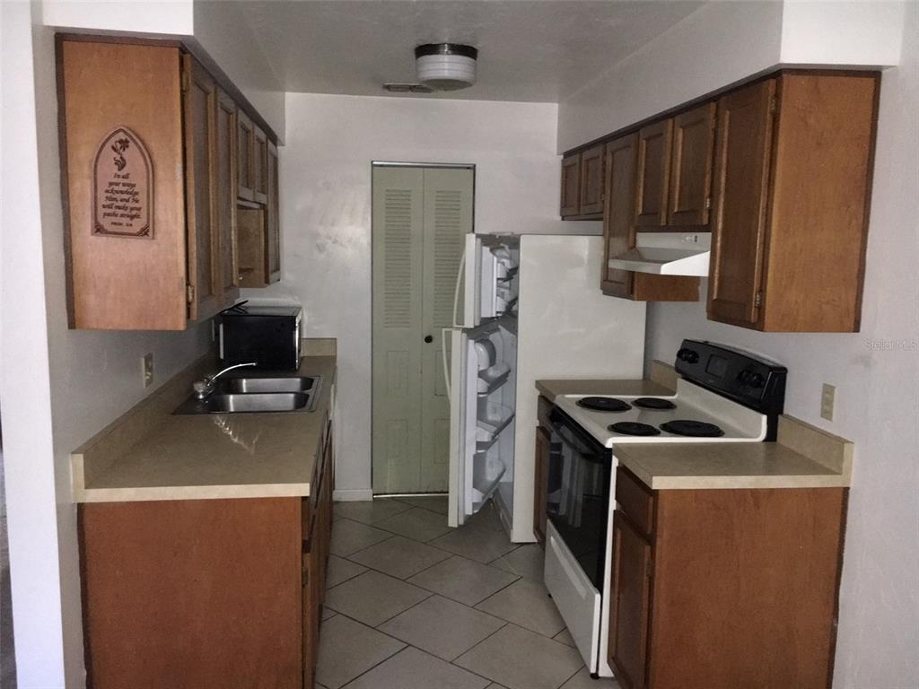 A galley kitchen features wood cabinets, laminate countertops, a white stove, and a refrigerator — 6735 SW 45TH AVENUE, GAINESVILLE, FL