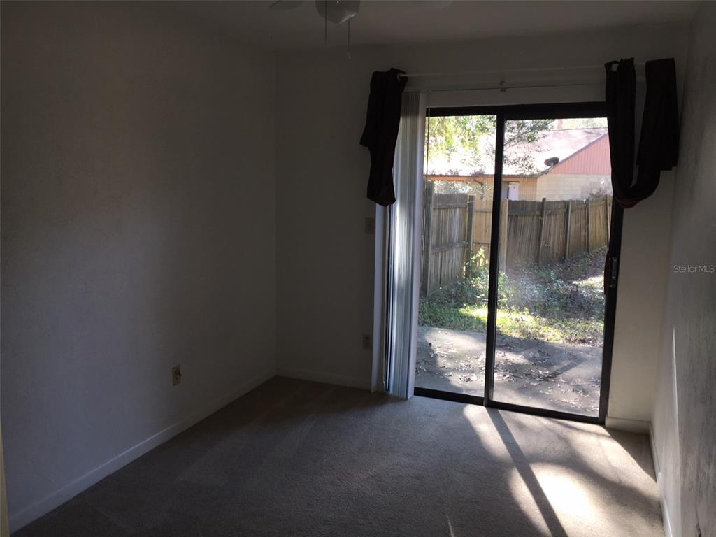 A carpeted room features a sliding glass door that opens to a fenced backyard — 6735 SW 45TH AVENUE, GAINESVILLE, FL