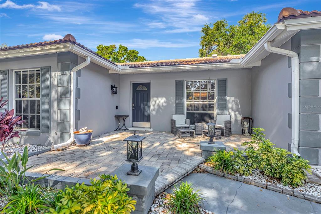A paved patio sits in front of a gray house with a dark blue door — 1424 STEWART BOULEVARD, CLEARWATER, FL