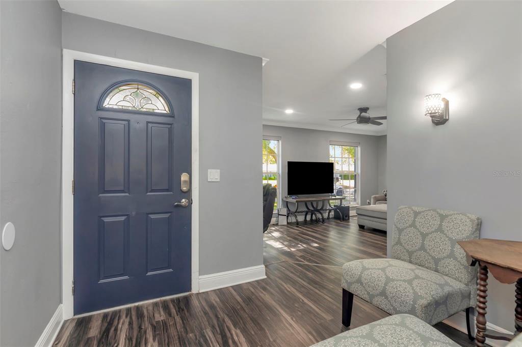 An entryway with a blue front door opens into a living room with wood flooring — 1424 STEWART BOULEVARD, CLEARWATER, FL