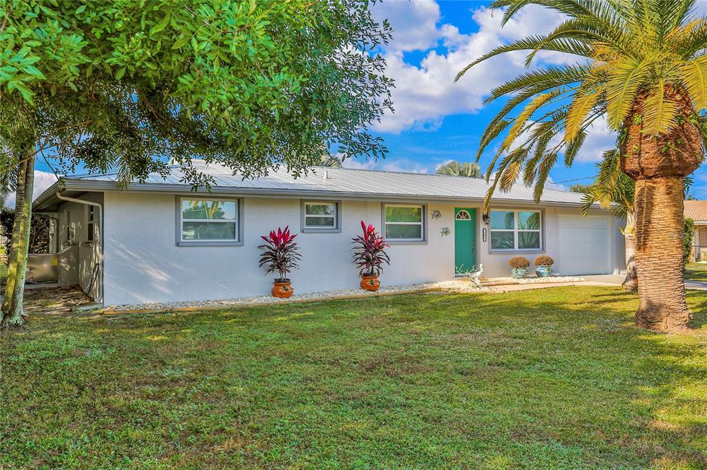 A single-story house with a white exterior, metal roof, green front door, and palm tree — 161 EASTON DRIVE NW, PORT CHARLOTTE, FL
