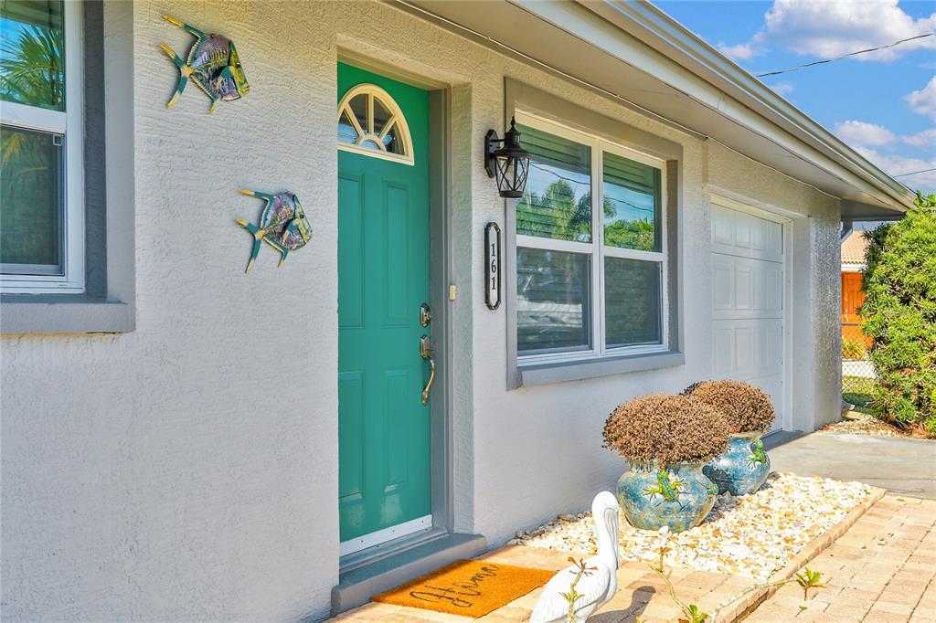 A teal front door with a decorative fish wall ornament and two potted plants outside — 161 EASTON DRIVE NW, PORT CHARLOTTE, FL