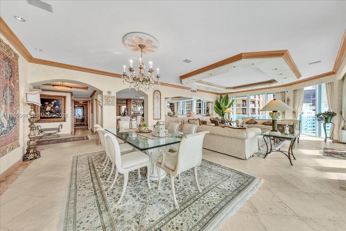 A formal dining and living area features a glass table, chandelier, and beige tile flooring — 10101 Collins Ave # 16B, Bal Harbour FL 33154, BAL HARBOUR, FL