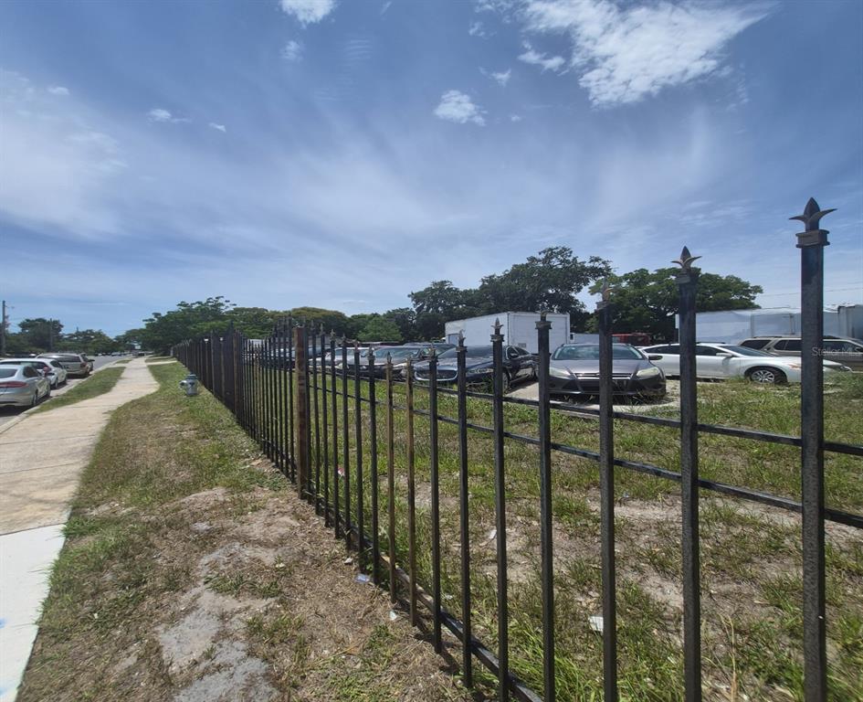 A black metal fence encloses a gravel lot filled with parked cars beside a sidewalk — 2000 S ORANGE BLOSSOM TRAIL, ORLANDO, FL