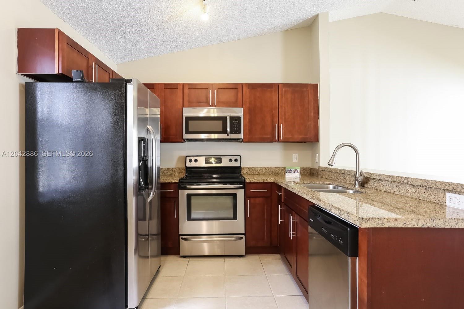 A kitchen features dark wood cabinets, granite countertops, and stainless steel appliances — PLANTATION, FL