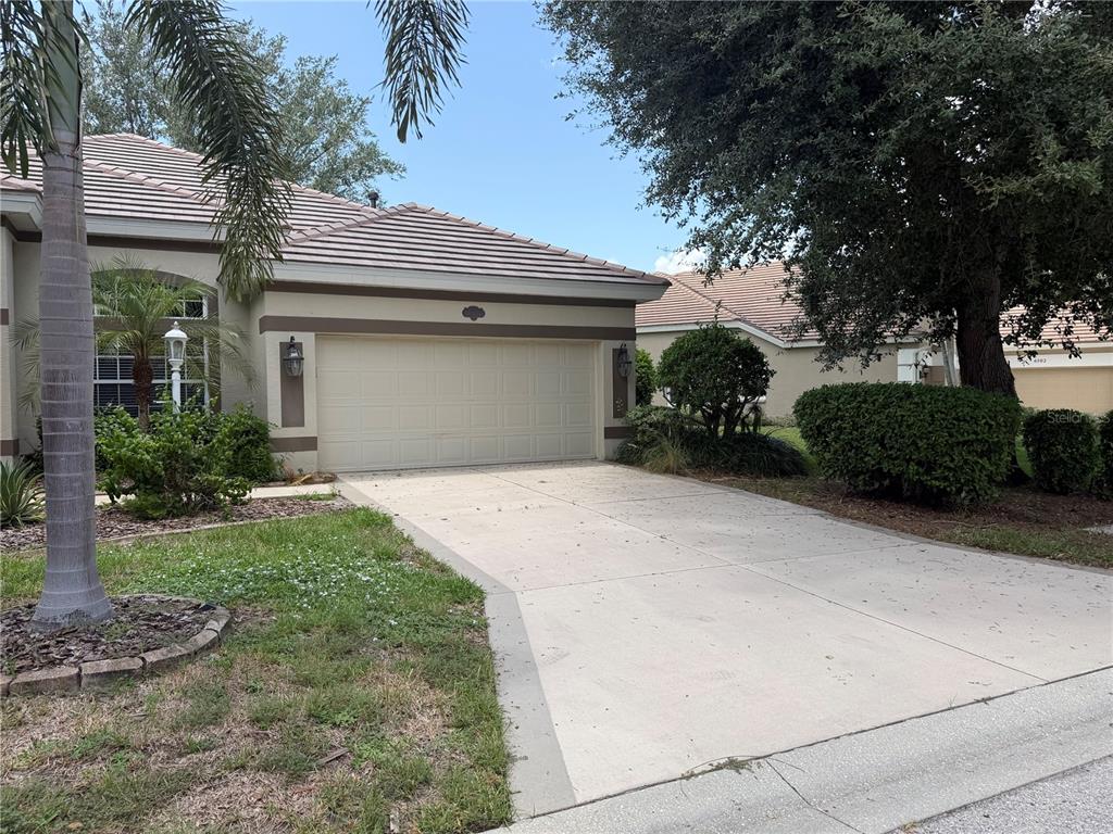 A beige house with a two-car garage and a concrete driveway under a clear sky — 6506 WATERS EDGE WAY, BRADENTON, FL