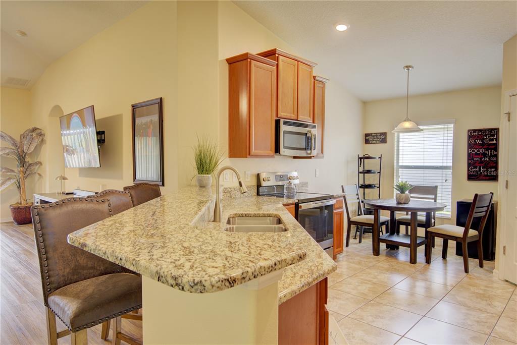 A kitchen features granite countertops, wood cabinets, stainless steel appliances, and an adjacent dining area — 4834 HAVILLAND DRIVE, MOUNT DORA, FL