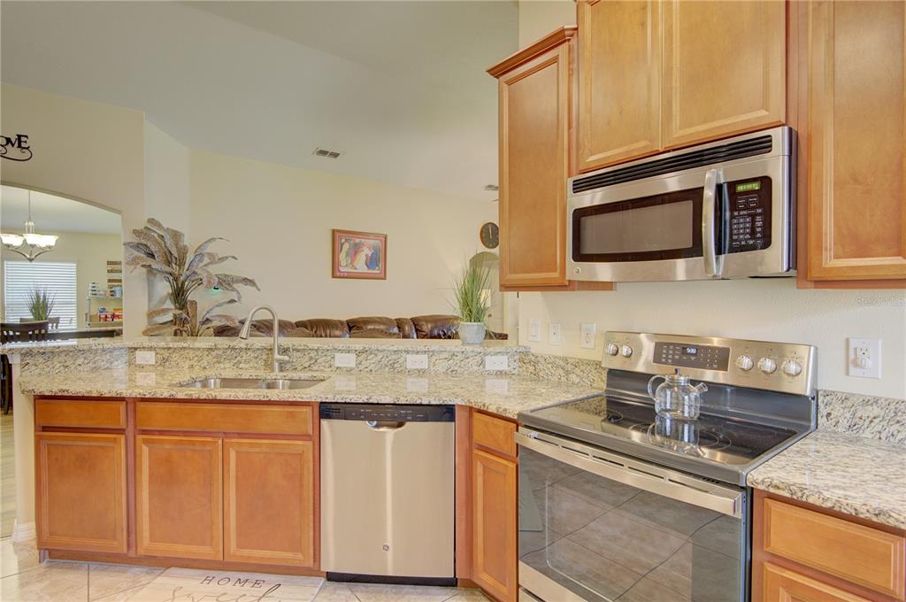 A kitchen with wood cabinets, granite countertops, and stainless steel appliances overlooks a living area — 4834 HAVILLAND DRIVE, MOUNT DORA, FL