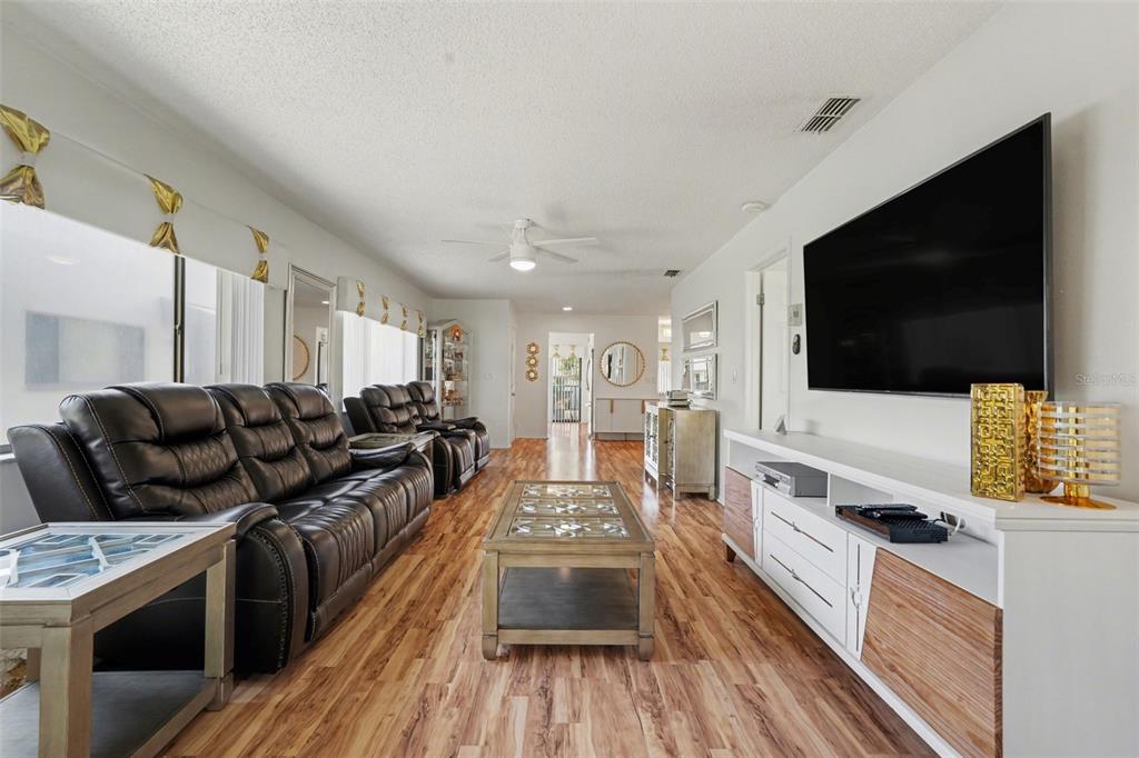 A living room features a dark leather sofa, wood-look flooring, and a wall-mounted television — 13006 WEDGEWOOD WAY UNIT D, HUDSON, FL