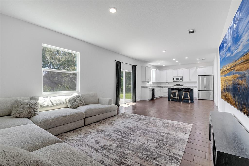 A living room with a sectional sofa and area rug opens to a modern kitchen — 651 PARAKEET COURT, KISSIMMEE, FL
