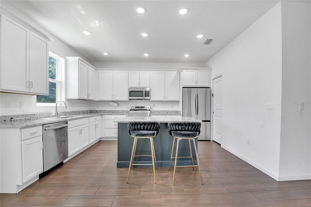A kitchen with white cabinets, granite countertops, a dark blue island, and stainless steel appliances — 651 PARAKEET COURT, KISSIMMEE, FL
