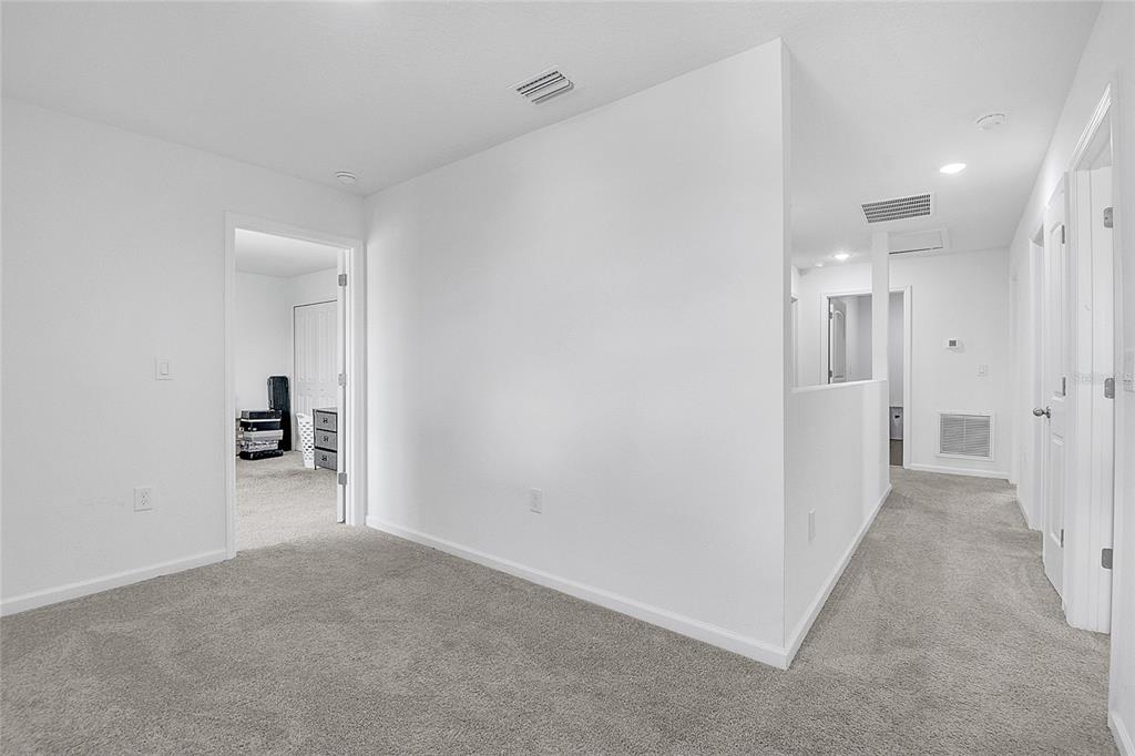 A carpeted hallway with white walls leads to several doorways and a small loft area — 651 PARAKEET COURT, KISSIMMEE, FL