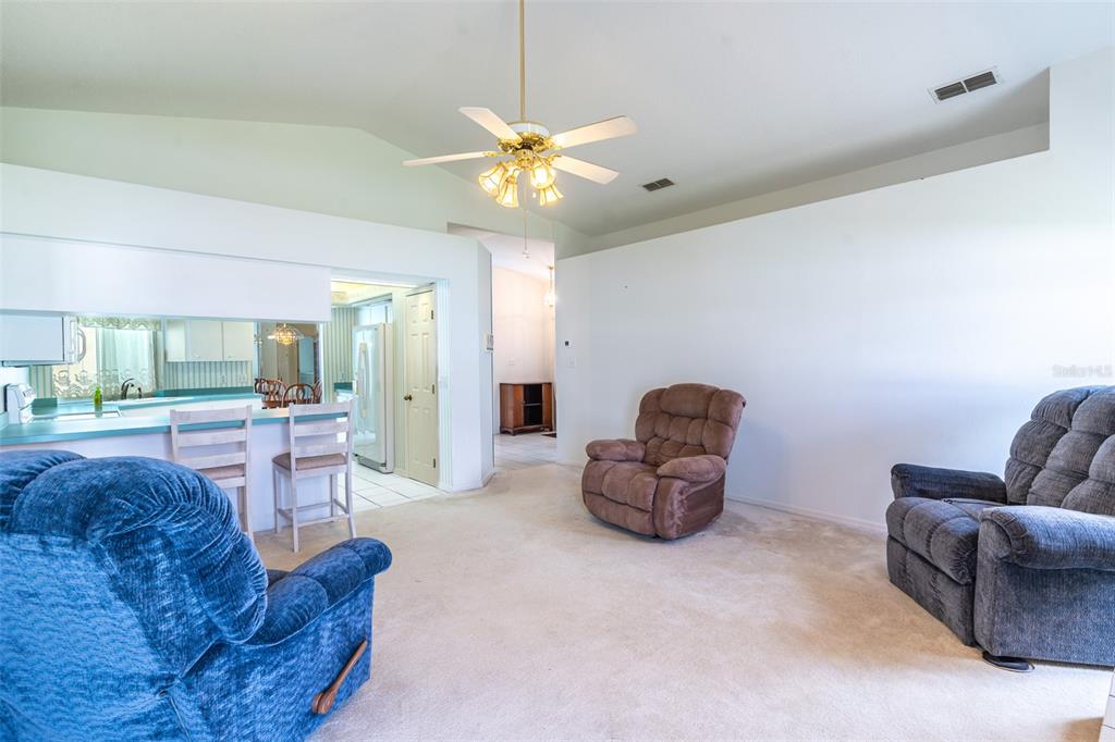 A living room with beige carpet, a ceiling fan, and three recliner chairs — 699 HUNTERS RUN BOULEVARD, LAKELAND, FL
