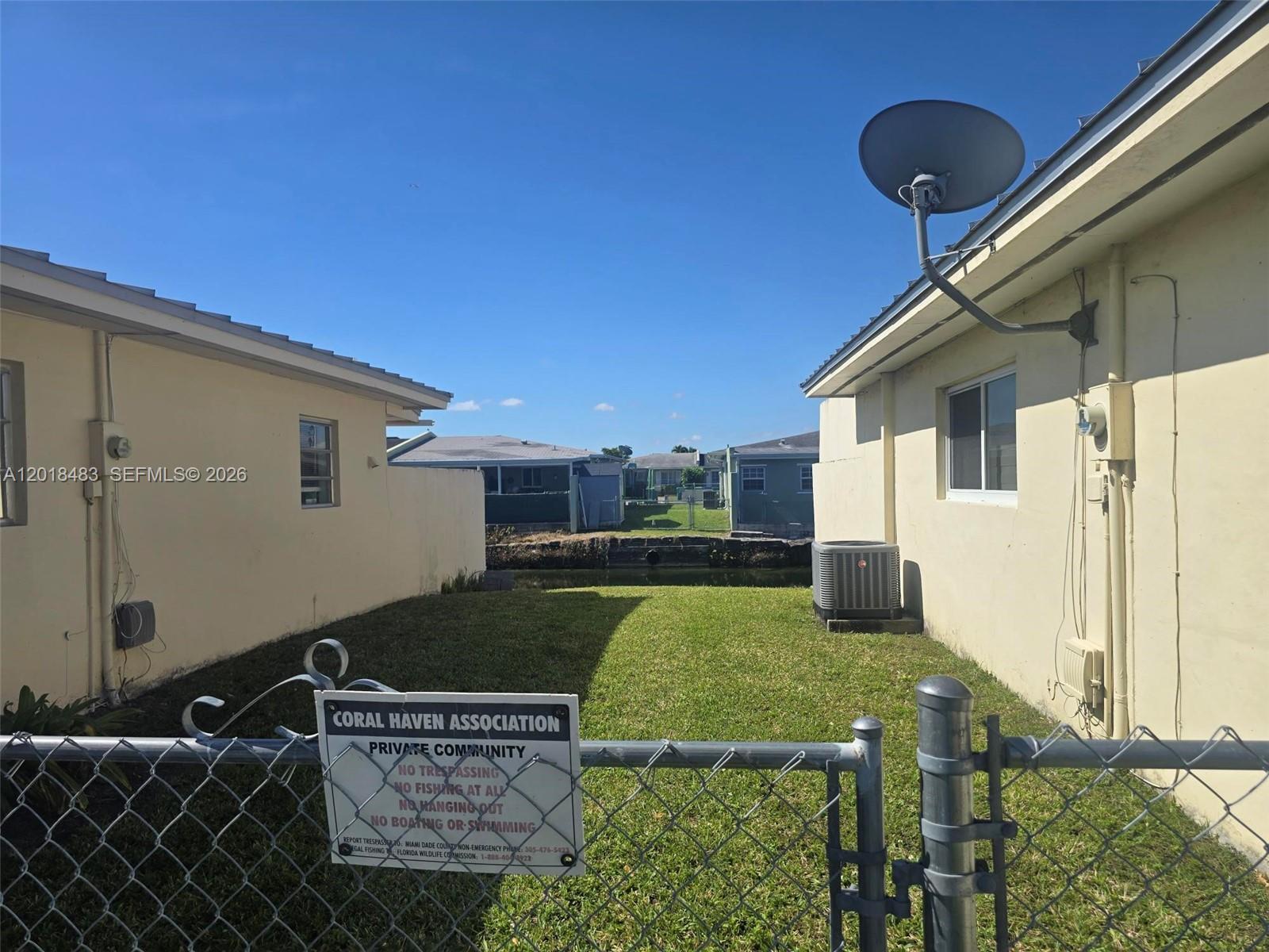 A grassy backyard sits between two houses with a canal and a chain-link fence — 10106 SW 20th St, Miami FL 33165, MIAMI, FL