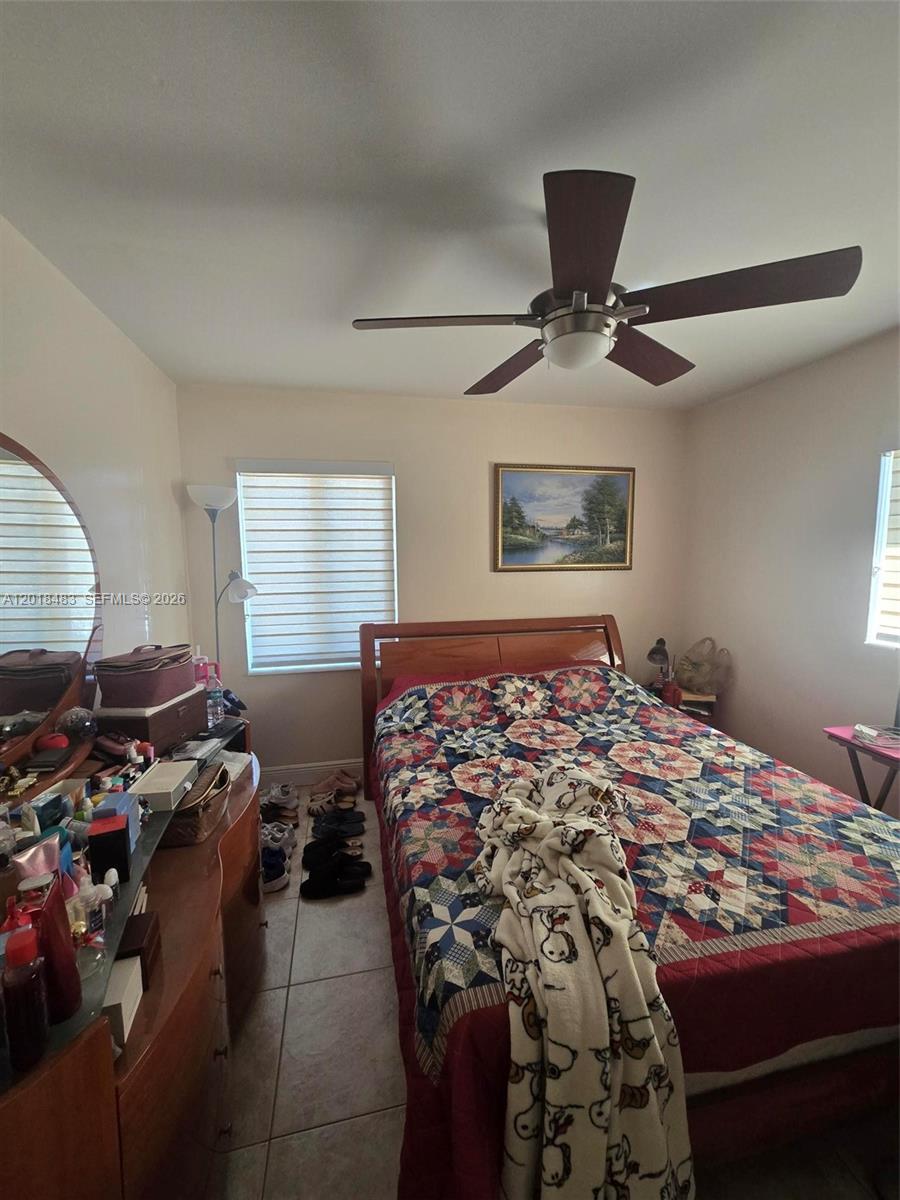 A bedroom features a wooden bed frame with a patterned quilt, a ceiling fan, and tile flooring — 10106 SW 20th St, Miami FL 33165, MIAMI, FL