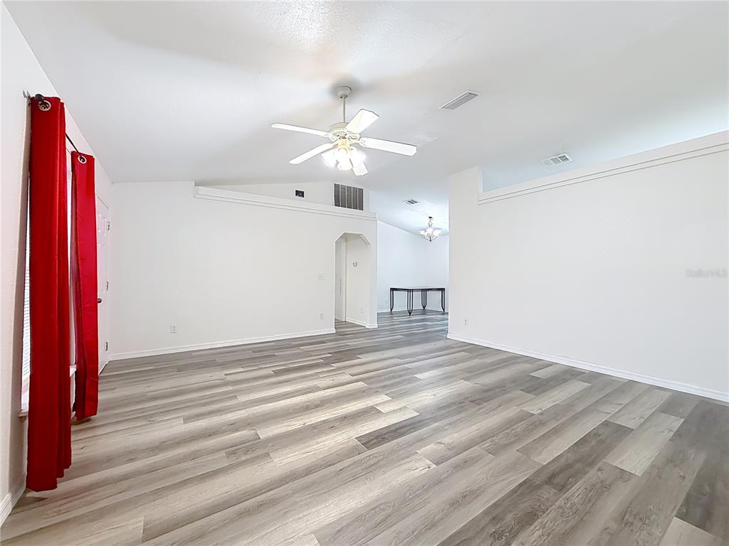 A spacious living room features white walls, vaulted ceilings, and grey wood-look laminate flooring — 13117 SW 33RD TERRACE, OCALA, FL
