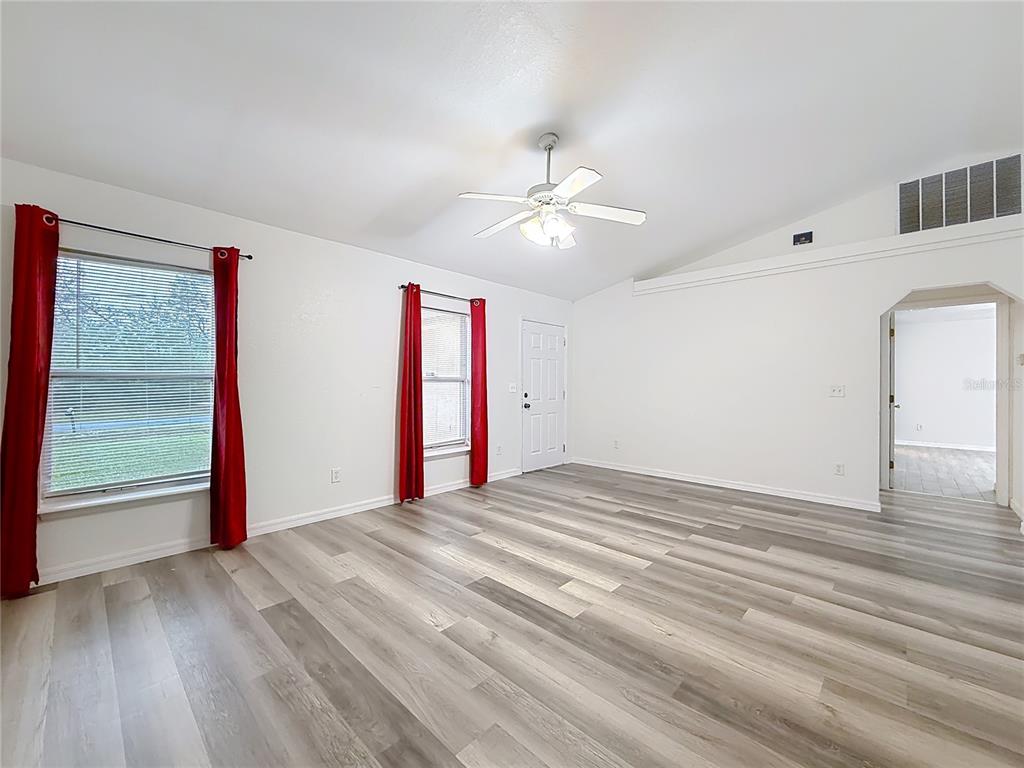 A living room with white walls, light wood-look flooring, two windows with red curtains, and a ceiling fan — 13117 SW 33RD TERRACE, OCALA, FL
