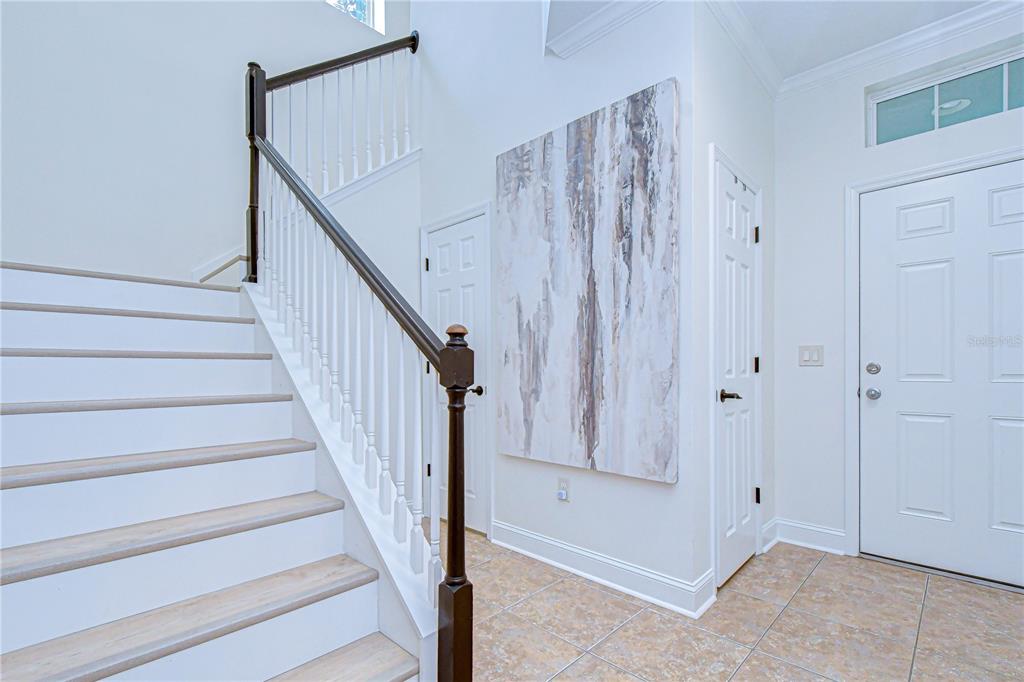 An entryway features a staircase with white risers, light wood treads, and a dark railing — 5301 MATCH POINT PLACE, LITHIA, FL