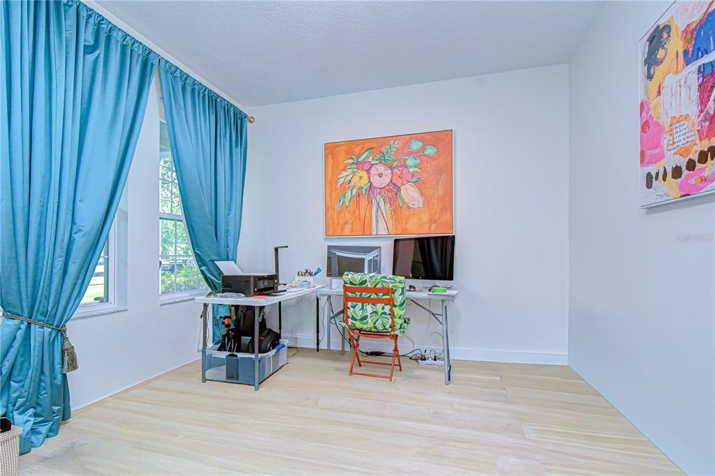 A home office features light wood-look flooring, teal curtains, and two desks with a chair — 5301 MATCH POINT PLACE, LITHIA, FL