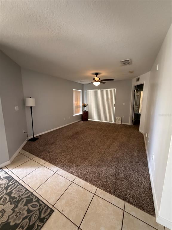 A living room features beige carpet, light gray walls, a ceiling fan, and sliding glass doors — 8819 GRAND PALMS CIRCLE UNIT A, KISSIMMEE, FL