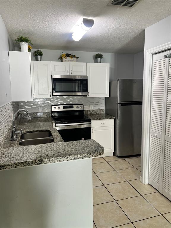A kitchen features white cabinets, stainless steel appliances, granite countertops, and light-colored tile flooring — 8819 GRAND PALMS CIRCLE UNIT A, KISSIMMEE, FL