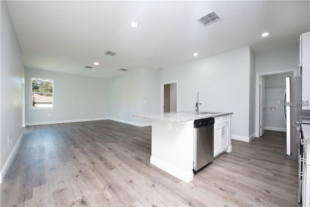 An open-concept kitchen and living area features light gray walls, wood-look flooring, and an island — 574 GERALDINE DRIVE, DELTONA, FL