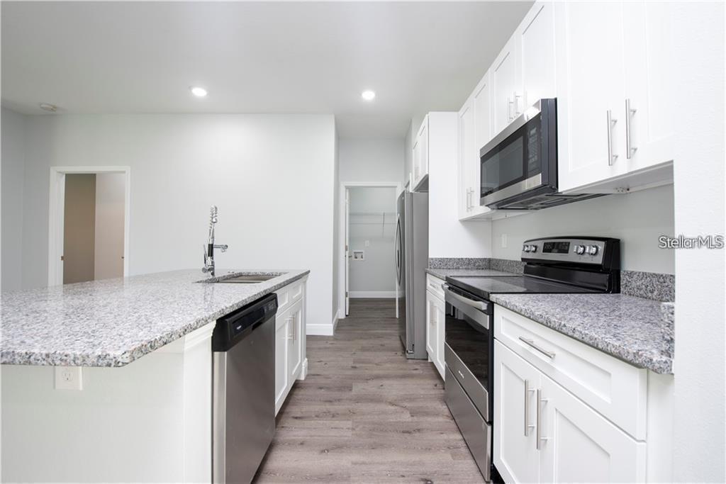 A kitchen features white cabinets, granite countertops, stainless steel appliances, and wood-look flooring — 574 GERALDINE DRIVE, DELTONA, FL