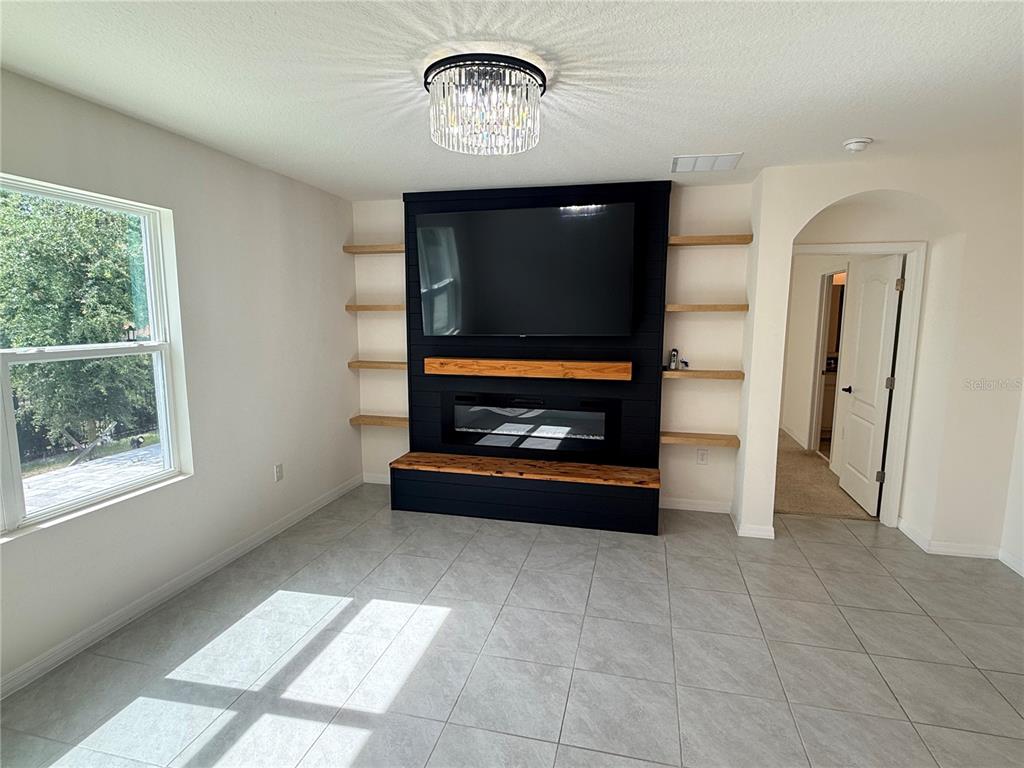 A living room features a black shiplap accent wall with a fireplace, television, and shelving — 2916 SUNRIDGE LOOP, ST CLOUD, FL